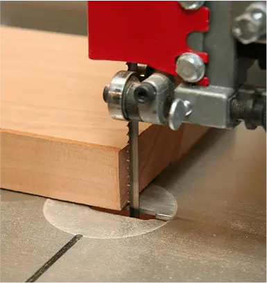 Band saw machine cutting a wooden block with a vertical metal blade in a workshop